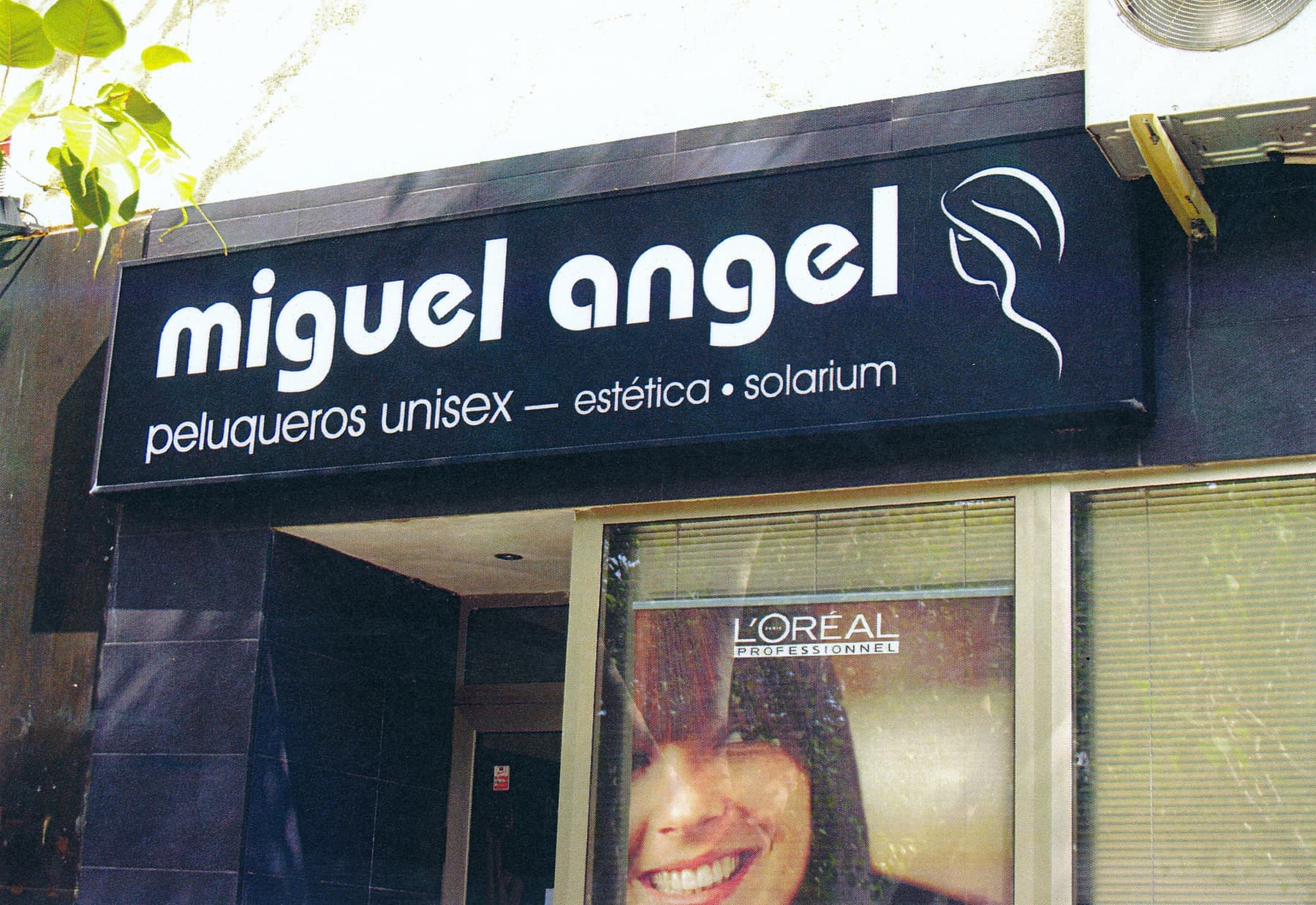 Rótulo negro de la peluquería Miguel Ángel con escaparate publicitario