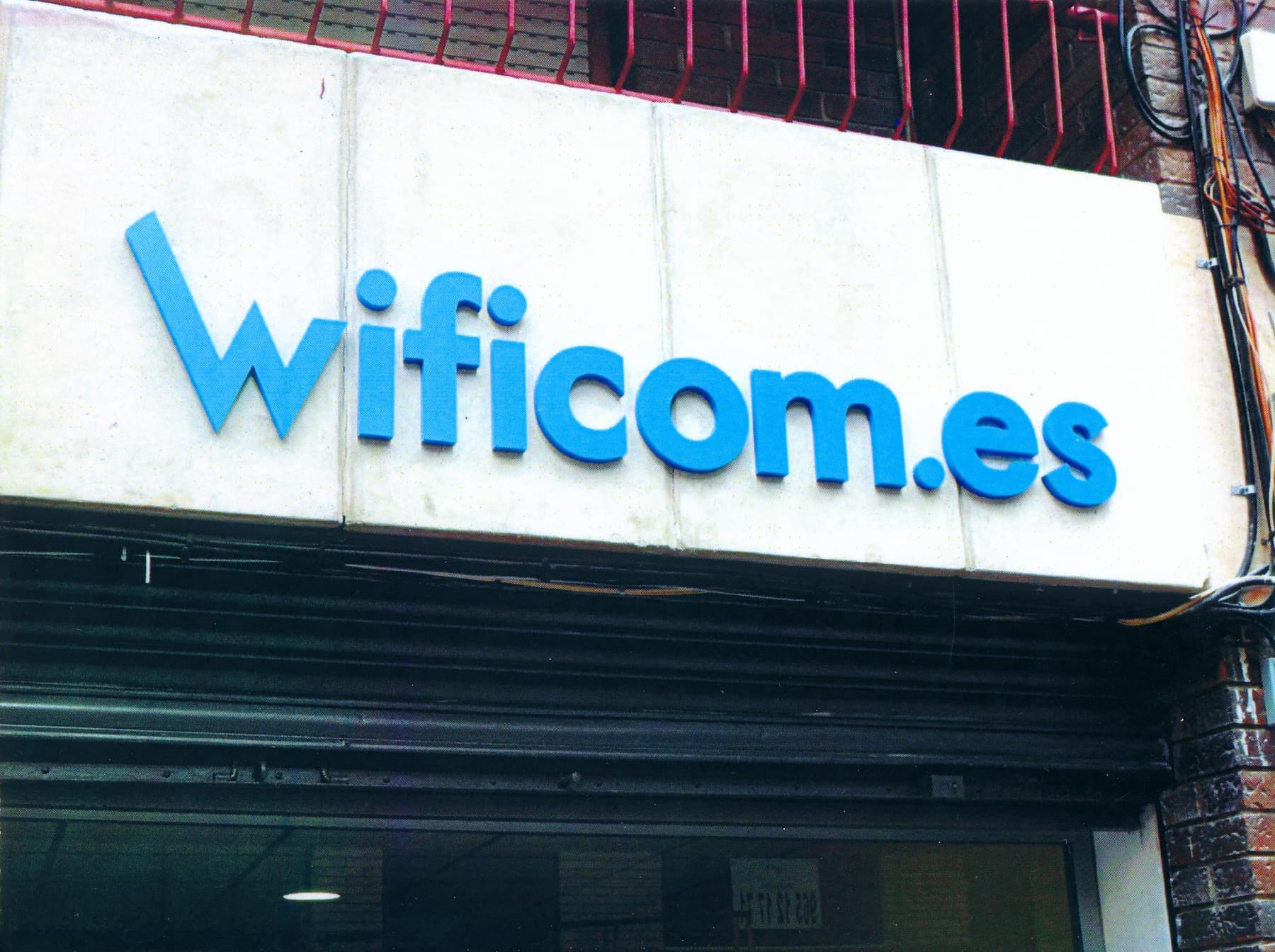 Rótulo blanco de Wificom.es con tipografía azul sobre la entrada del local